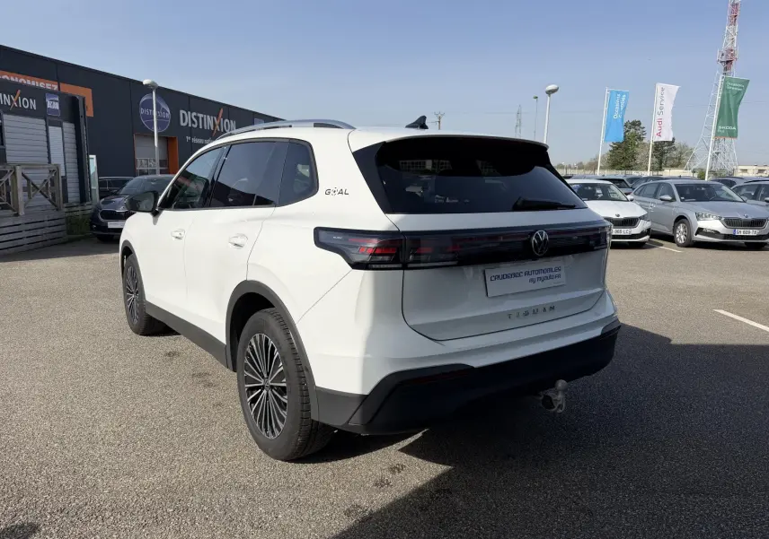 Vue 3/4 arrière droite d’un Volkswagen Tiguan blanc avec attelage rabattable et jantes alliage noires brillantes.