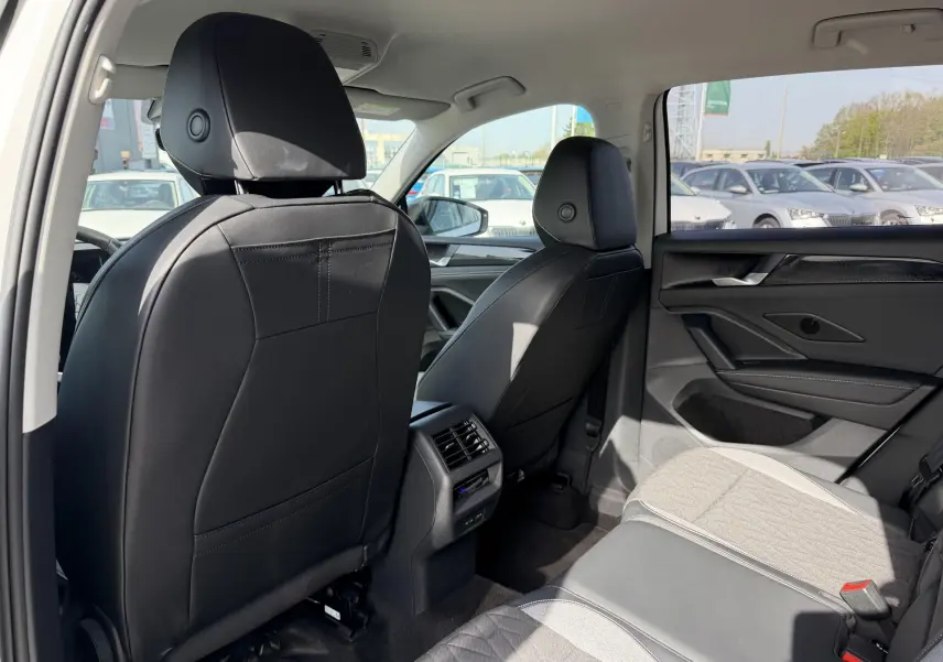 Vue intérieure arrière droite du Volkswagen Tiguan blanc 2025, sièges avant cuir noir et banquette tissu gris.