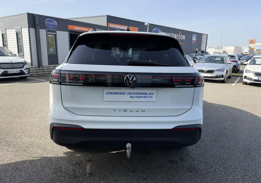 Vue arrière d'un Volkswagen Tiguan blanc avec attelage rabattable et feux arrière LED noirs, sur parking extérieur.