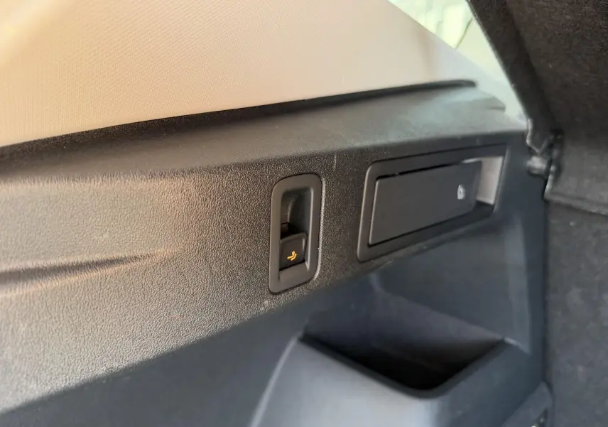 Gros plan sur la commande de rabattement des sièges dans le coffre du Volkswagen Tiguan blanc, intérieur noir.