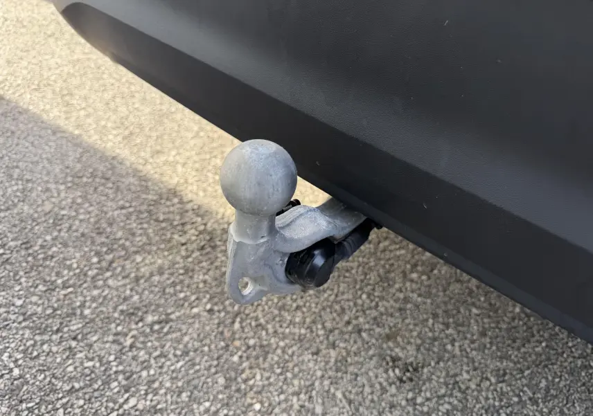 Gros plan sur l'attelage rabattable gris fixé sous le pare-chocs arrière noir du Volkswagen Tiguan blanc.