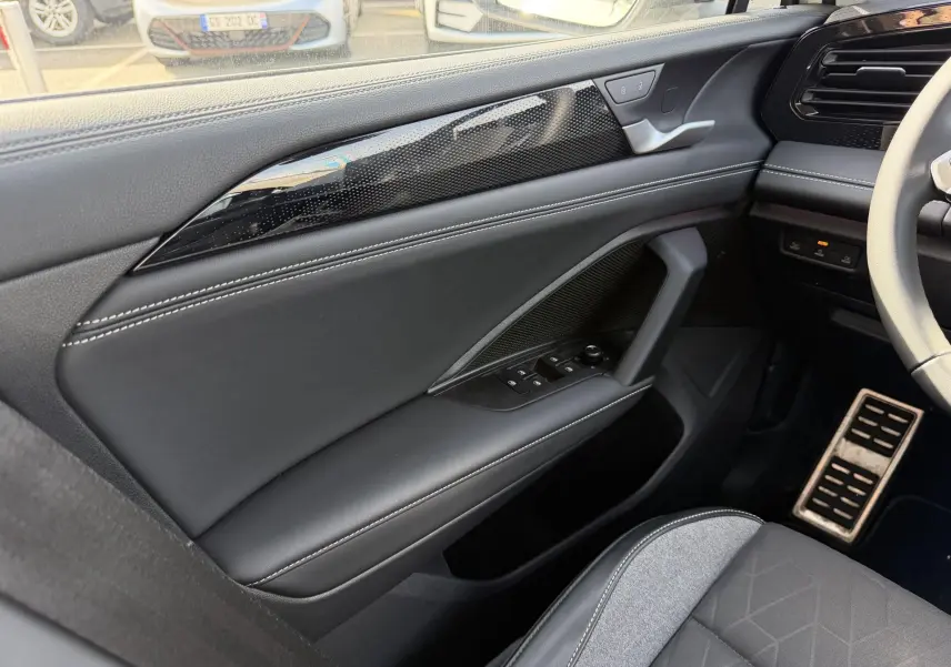 Vue intérieure côté conducteur du Volkswagen Tiguan 2025, porte noire avec surpiqûres blanches et commandes électriques.