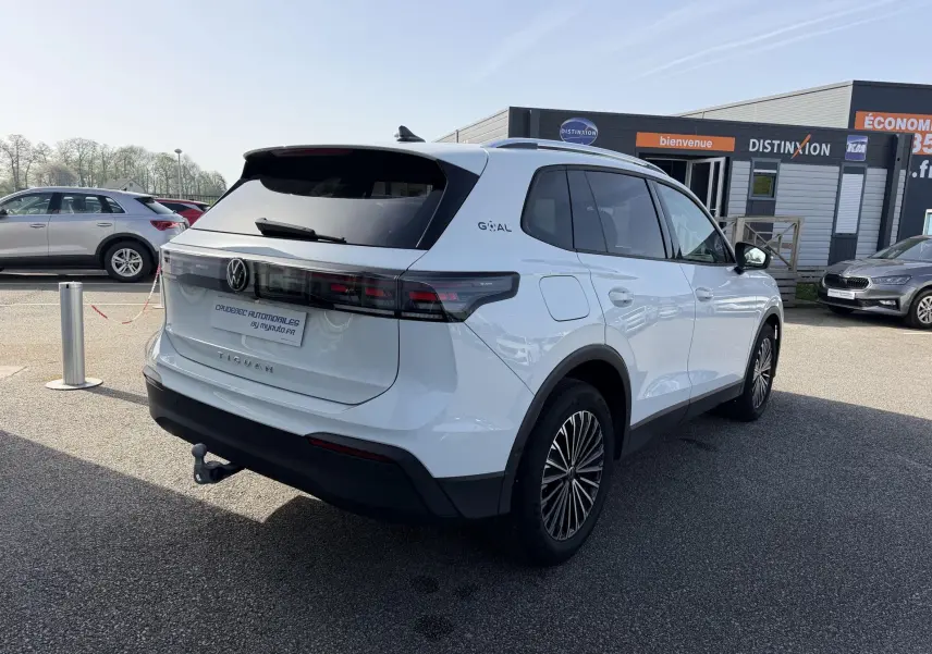 Vue 3/4 arrière droite d’un Volkswagen Tiguan blanc avec attelage et jantes alliage noir brillant, stationné en extérieur.