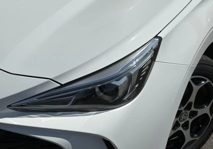 Gros plan sur le phare avant droit et la roue alliage 16'' d’un MG3 blanc Dover 2025.