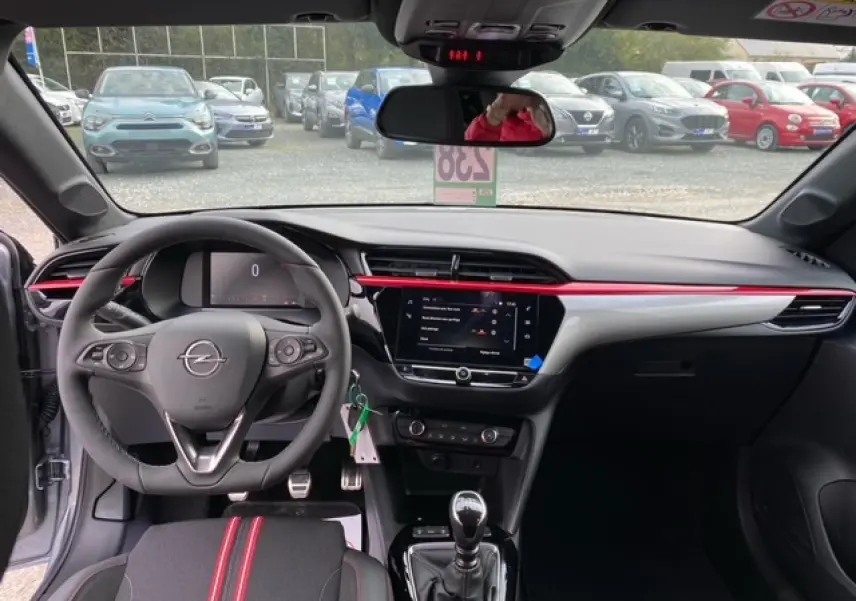 Intérieur avant de l'Opel Corsa gris magnetic 2022, volant multifonction, écran tactile 7 pouces et sellerie noire avec bandes rouges.