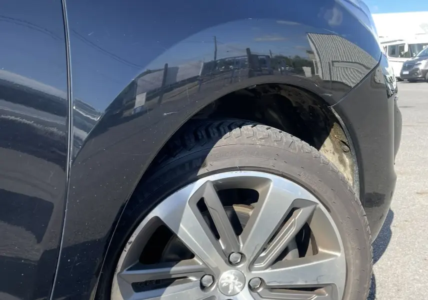 Gros plan sur la roue avant droite d’un Peugeot 3008 noir, mettant en valeur la jante alliage au soleil.