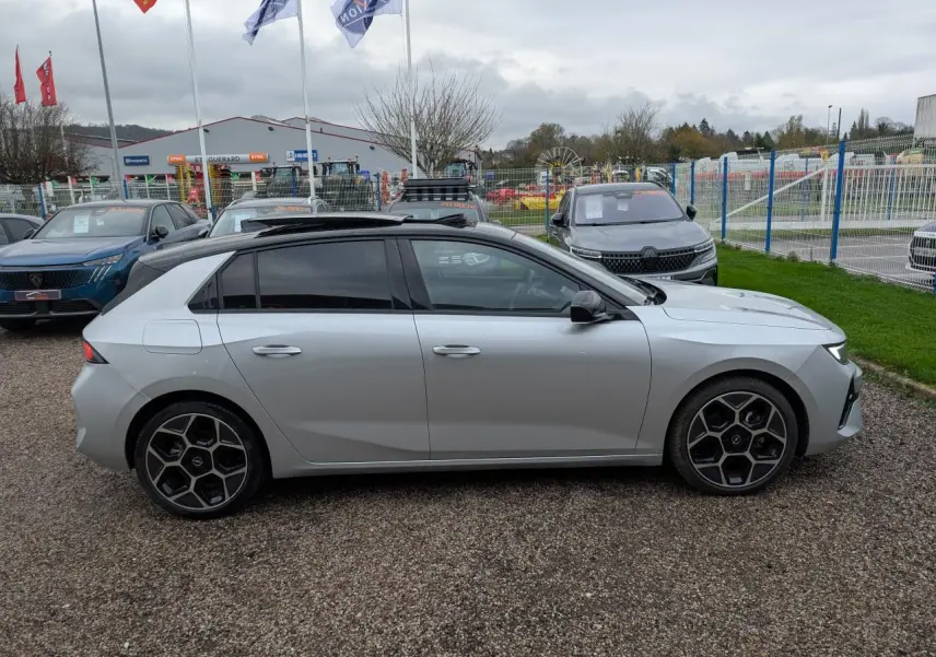 Profil droit d'une Opel Astra gris métallisé avec toit ouvrant panoramique et jantes alliage 18 pouces pentagonales diamantées.