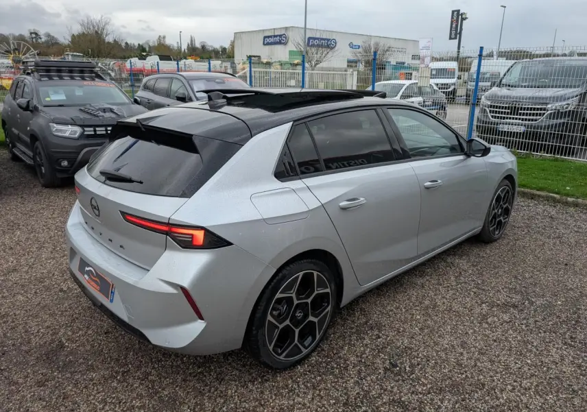Opel Astra 2024 gris métallisé vue 3/4 arrière droit avec toit noir et jantes alliage 18 pouces pentagonales.