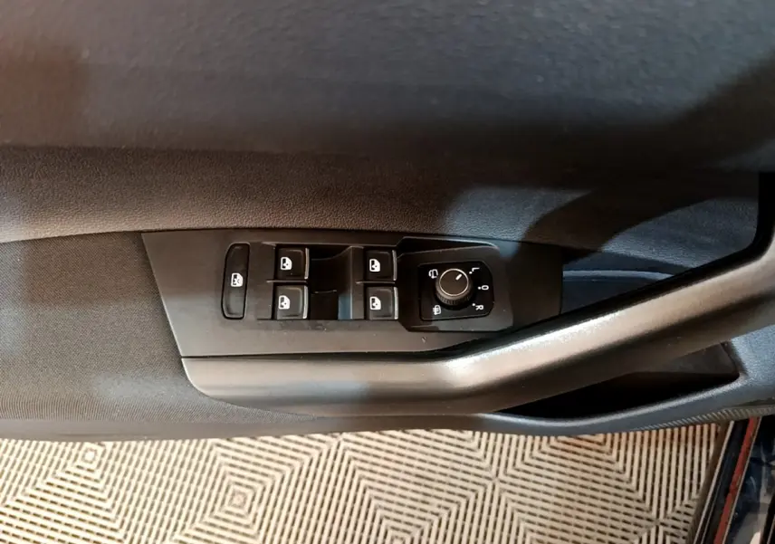 Vue rapprochée sur le panneau de commandes des vitres et rétroviseurs côté conducteur d’un Volkswagen Taigo noir 2023.