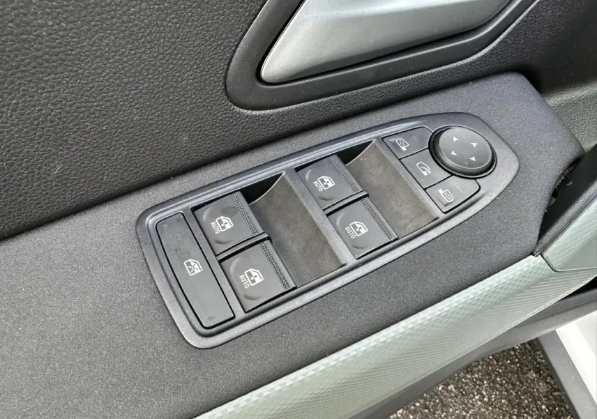 Gros plan sur les commandes des vitres et rétroviseurs côté conducteur du Dacia Duster blanc glacier 2025.
