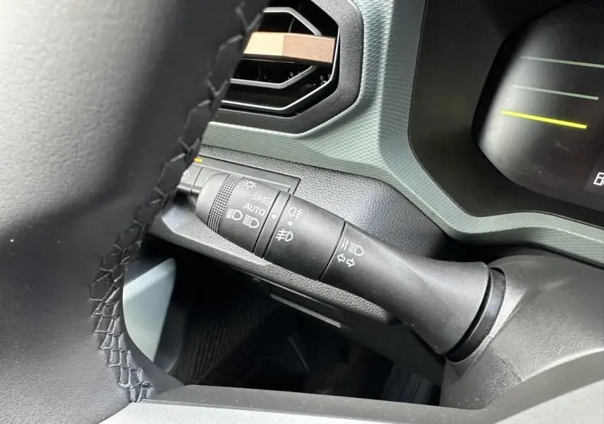 Gros plan sur la commande des feux et clignotants à gauche du volant dans l’habitacle du Dacia Duster blanc glacier 2025.