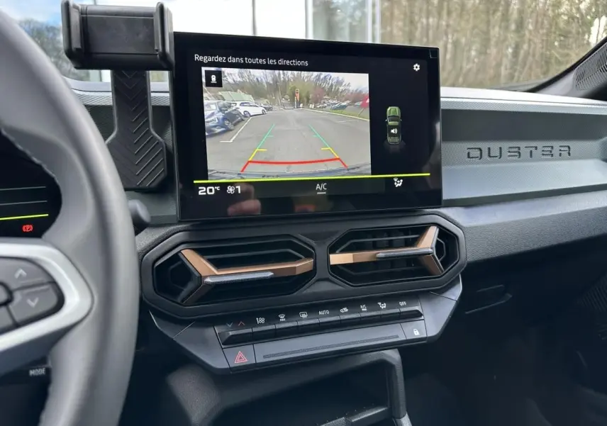 Vue intérieure du tableau de bord du Dacia Duster 2025 avec écran tactile et aérateurs hexagonaux cuivrés.