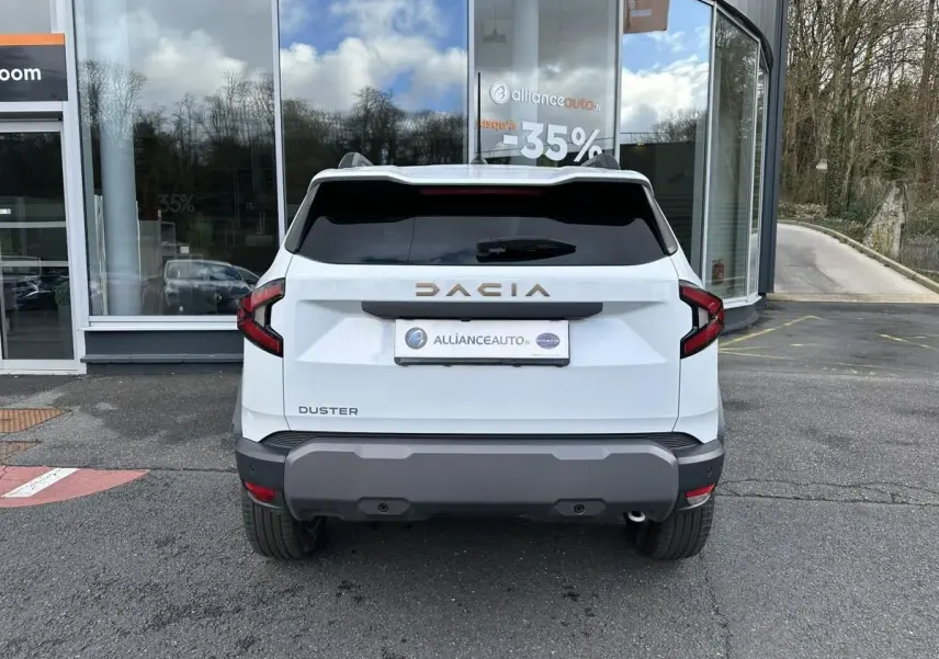 Vue arrière du Dacia Duster blanc glacier 2025 avec vitres surteintées et logo DACIA en relief doré.