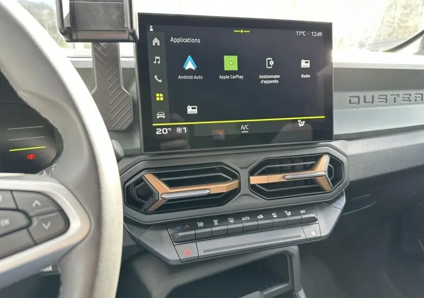 Vue intérieure du tableau de bord du Dacia Duster 2025, avec écran tactile central et aérateurs hexagonaux bronze.