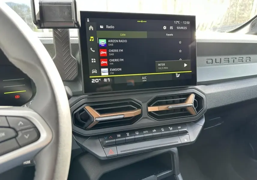 Vue intérieure du tableau de bord du Dacia Duster 2025, avec écran tactile central et aérateurs hexagonaux bronze.
