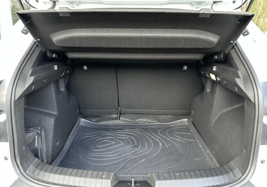 Coffre ouvert vu de l'arrière d'un Dacia Duster blanc glacier, avec tapis de sol noir et intérieur sombre.