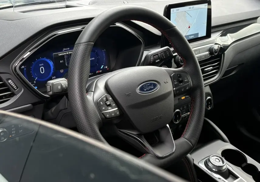 Vue intérieure centrée sur le volant noir perforé avec surpiqûres rouges et l’écran tactile du tableau de bord du Ford Kuga.