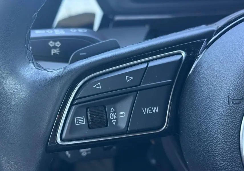 Gros plan sur les commandes multifonctions côté gauche du volant cuir de l'Audi A3 Sportback 2024.