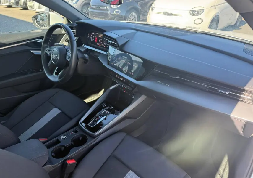 Vue intérieure côté conducteur de l'Audi A3 Sportback 2024, avec tableau de bord noir et écran tactile central.