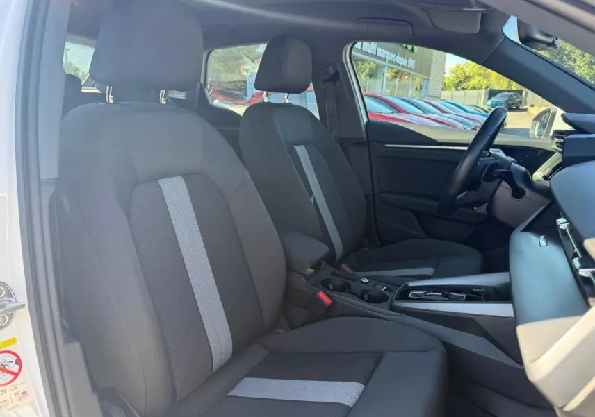 Vue intérieure côté conducteur de l'Audi A3 Sportback 2024, sièges tissu noir avec bande grise centrale et console moderne.