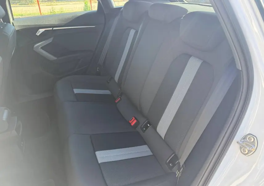 Vue intérieure côté droit des sièges arrière en tissu noir avec bandes grises de l'Audi A3 Sportback 2024 blanche.