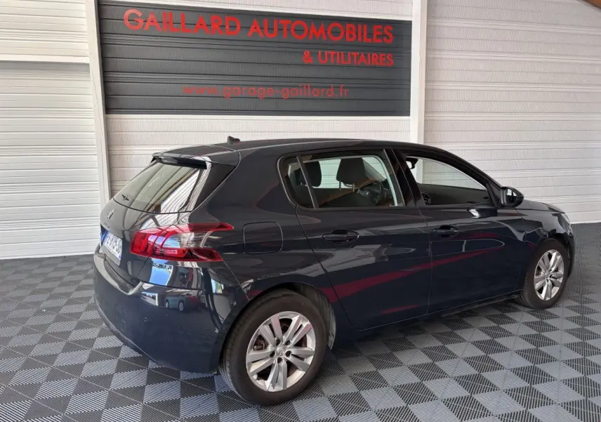 Vue 3/4 arrière droite d'une Peugeot 308 gris foncé garée en intérieur sur sol à damier.