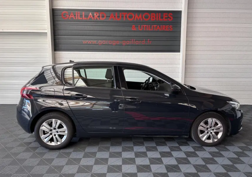 Profil côté gauche d'une Peugeot 308 gris foncé de 2019 garée en intérieur sur sol damier.