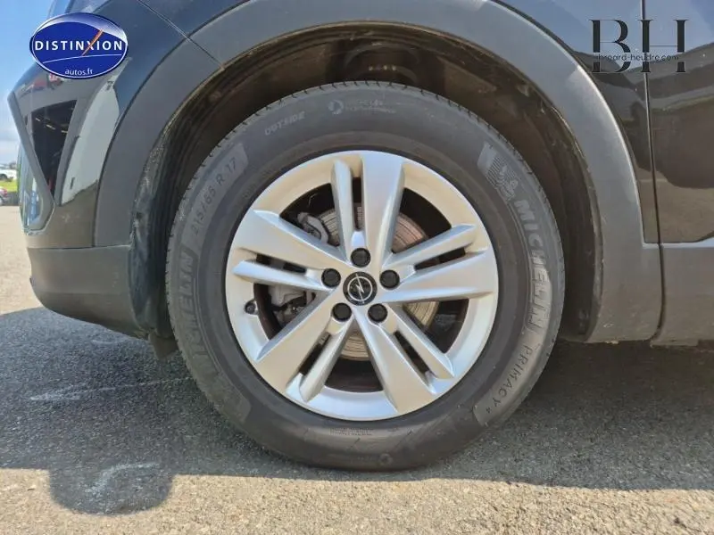 Gros plan sur la roue avant gauche de l'Opel Grandland noir Karbon Métallisé avec jante alu et logo Opel visible au centre.