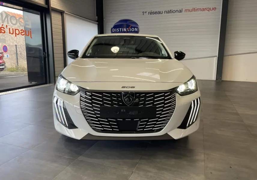 Vue frontale d'une Peugeot 208 blanche Okenite avec calandre noire et feux diurnes à LED en griffes allumés.