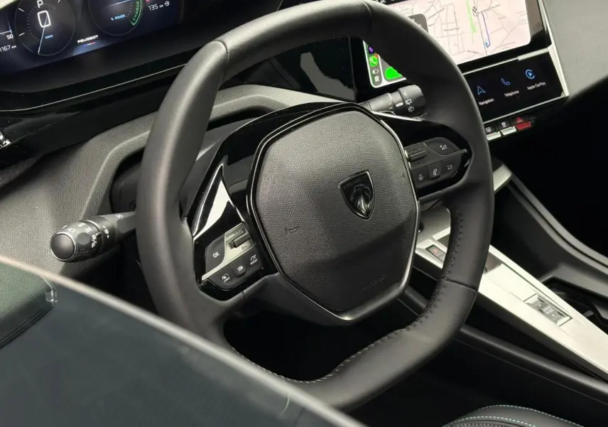 Vue rapprochée du volant noir du Peugeot 308 SW Hybrid 2025 avec tableau de bord numérique et écran tactile.