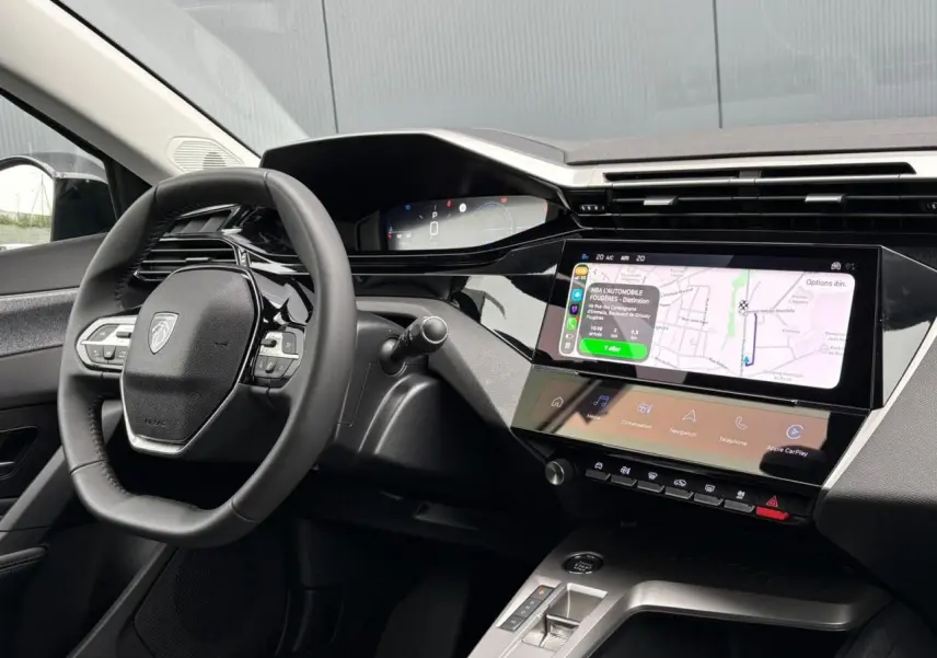 Vue intérieure côté conducteur du tableau de bord noir et écran tactile affichant la navigation du Peugeot 308 SW Hybrid 2025.