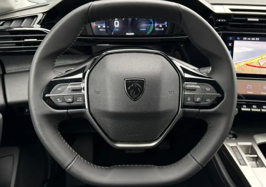 Vue rapprochée du volant cuir noir de la Peugeot 308 SW Hybrid 2025 avec commandes intégrées et tableau de bord numérique.