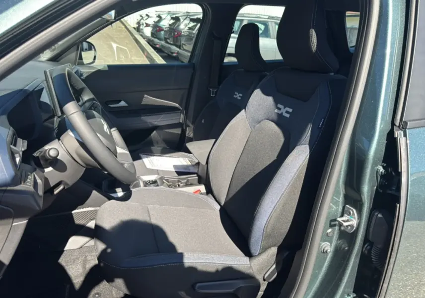 Vue intérieure côté conducteur du Dacia Bigster vert cèdre, montrant les sièges avant avec logo DC et volant cuir soft feel.