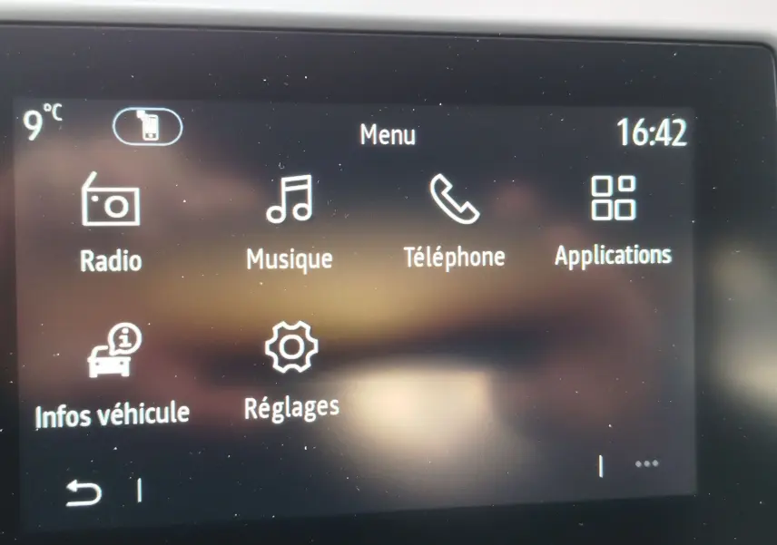 Écran tactile central de la Renault Clio rouge flamme 2025 affichant le menu principal avec options multimédia et réglages.