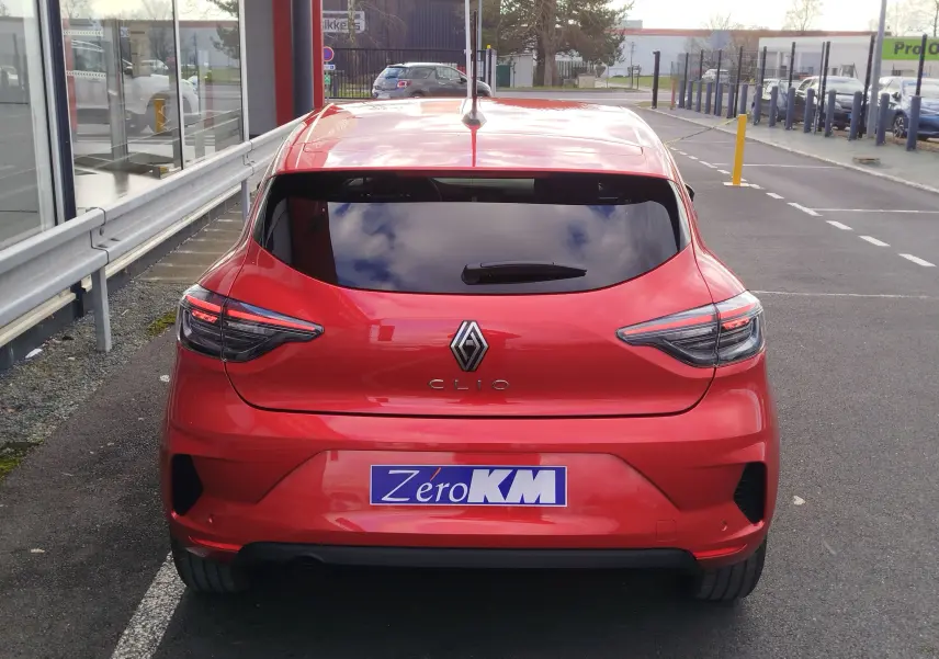 Vue arrière d'une Renault Clio rouge flamme 2025 avec feux LED et vitres arrière teintées sur parking urbain.