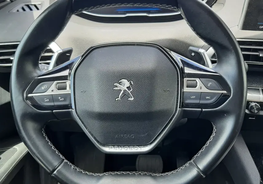 Volant en cuir noir avec commandes intégrées et logo Peugeot au centre dans un Peugeot 3008 gris de 2020.
