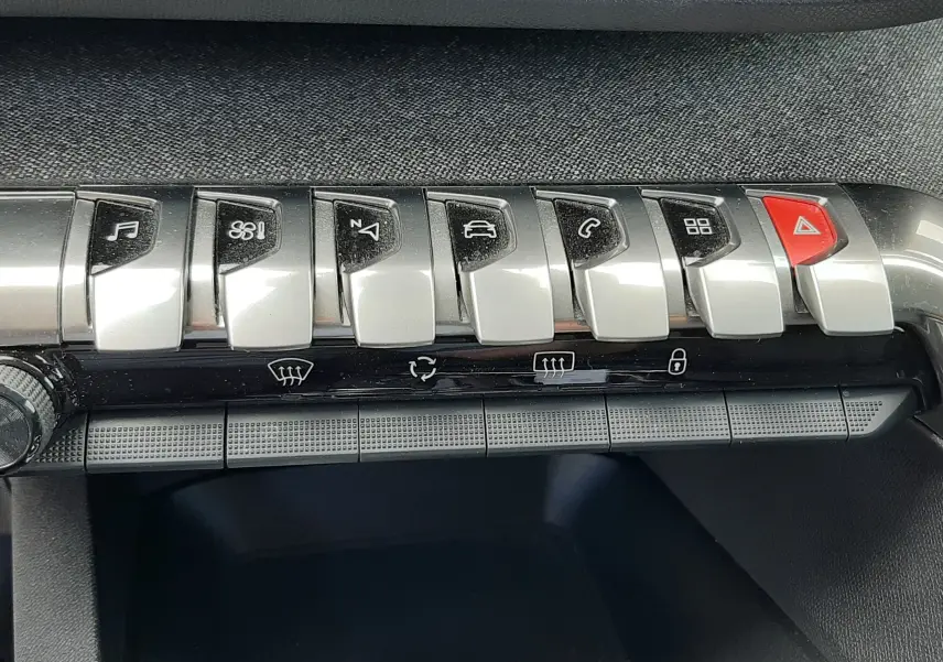 Gros plan sur la rangée de boutons argentés et noirs du tableau de bord du Peugeot 3008 gris, avec bouton rouge d'alerte.