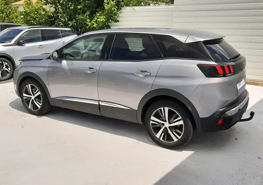 Peugeot 3008 gris en vue latérale droite, mettant en valeur ses feux arrière à trois griffes rouges et ses jantes bicolores.