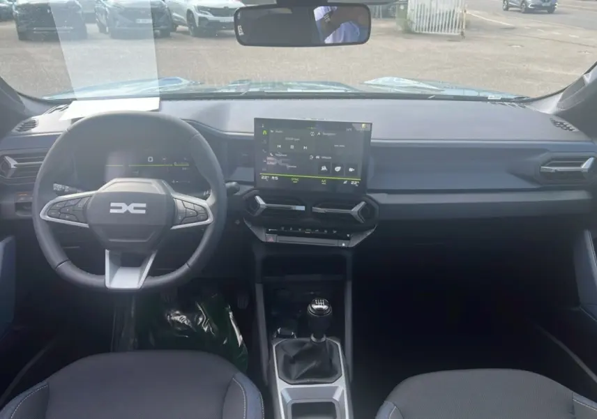 Vue intérieure frontale du tableau de bord du Dacia Bigster vert cèdre 2025 avec volant multifonction et écran tactile central.