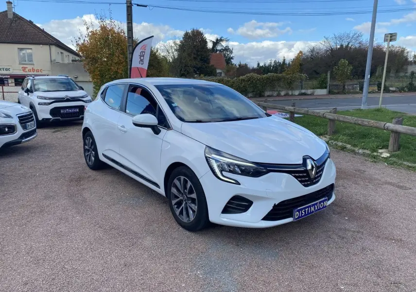Renault Clio blanc vue 3/4 avant droit, avec phares LED et jantes alliage, stationnée sur un parking extérieur.