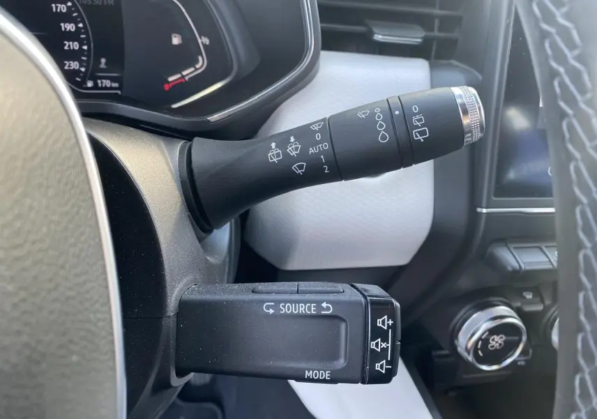 Détail des commandes au volant de la Renault Clio blanche 2021, avec commandes essuie-glaces et multimédia visibles.