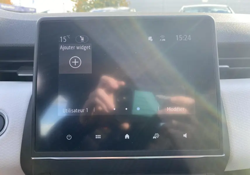 Écran tactile central du tableau de bord de la Renault Clio blanche, affichant l'interface utilisateur avec reflet solaire.