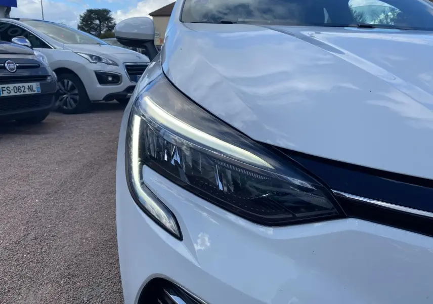 Gros plan sur le phare avant gauche LED d'une Renault Clio blanche 2021, soulignant son design moderne.