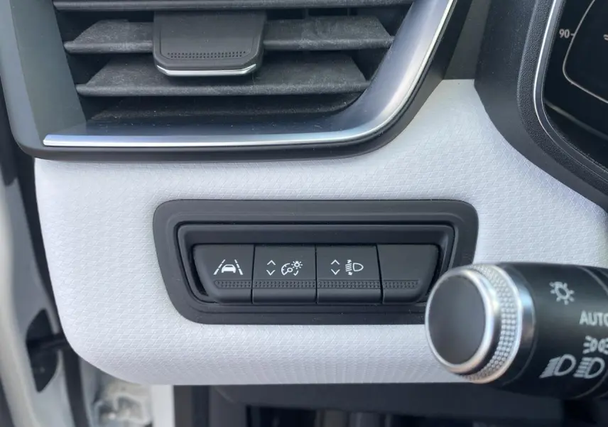 Gros plan sur les boutons de réglage d'aide à la conduite et éclairage dans l'habitacle blanc d'une Renault Clio 2021.