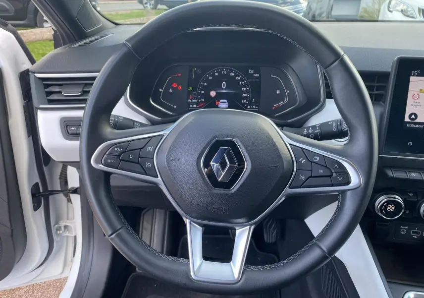 Vue centrée sur le volant noir de la Renault Clio blanche 2021, avec tableau de bord numérique et commandes intégrées.