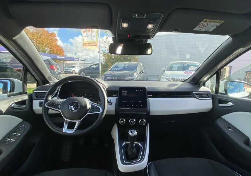 Vue intérieure avant de la Renault Clio blanche 2021, tableau de bord moderne avec écran tactile et volant multifonction.