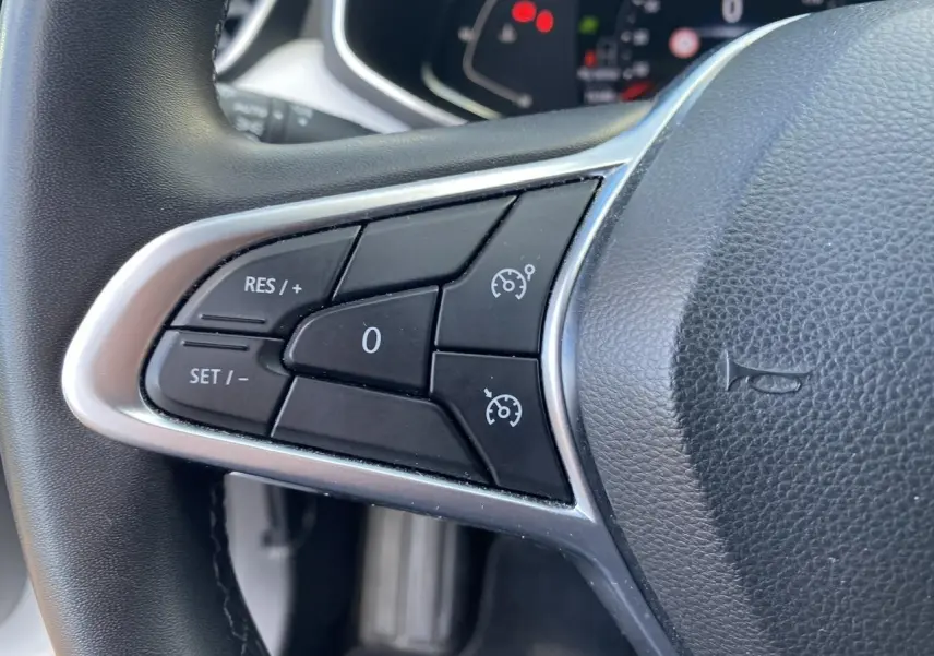 Gros plan sur les commandes du régulateur de vitesse au volant noir de la Renault Clio blanche 2021.