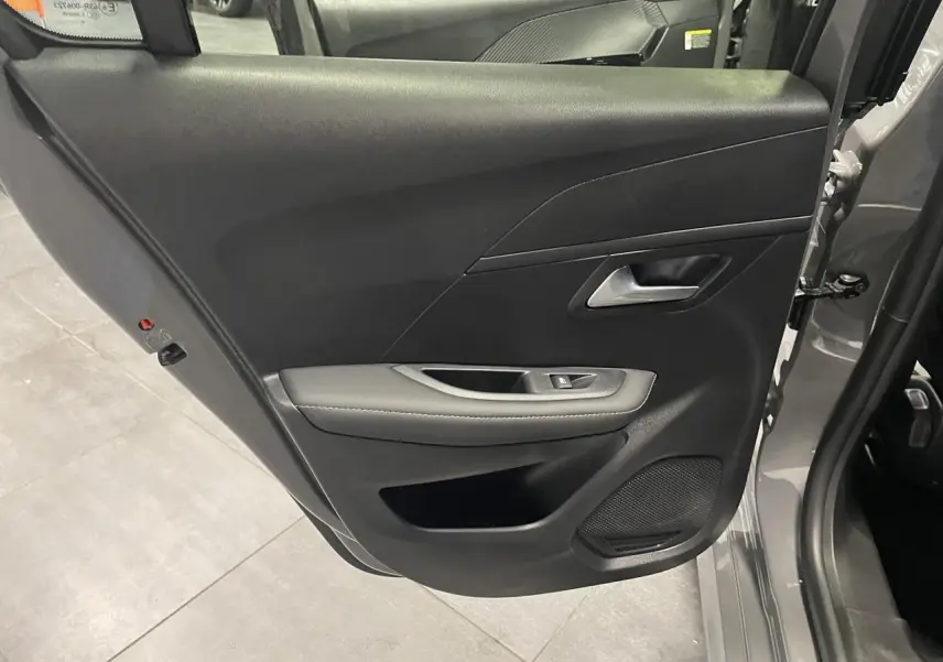 Porte arrière gauche ouverte d'une Peugeot 208 gris selenium, montrant la garniture noire avec accoudoir et haut-parleur intégré.