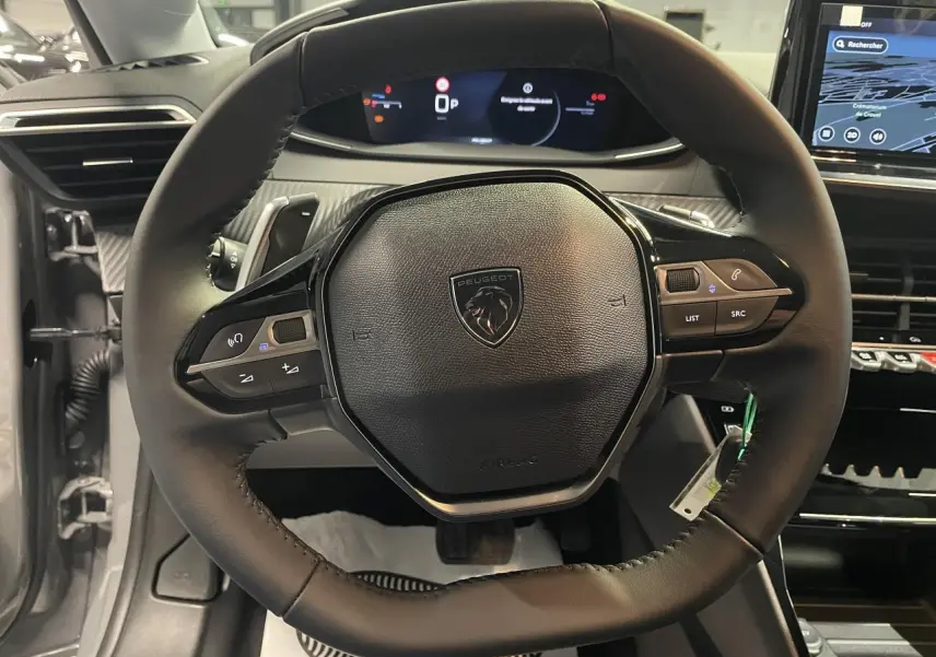 Vue rapprochée du volant cuir noir de la Peugeot 208 2025 avec commandes intégrées et tableau de bord numérique.