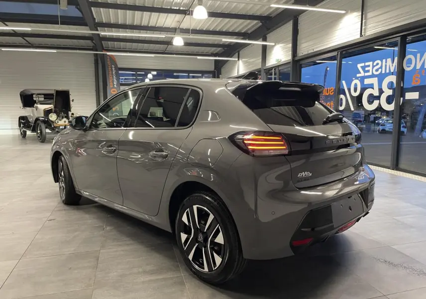 Vue 3/4 arrière droite d'une Peugeot 208 gris selenium avec feux arrière allumés et jantes alliage bi-tons en showroom.